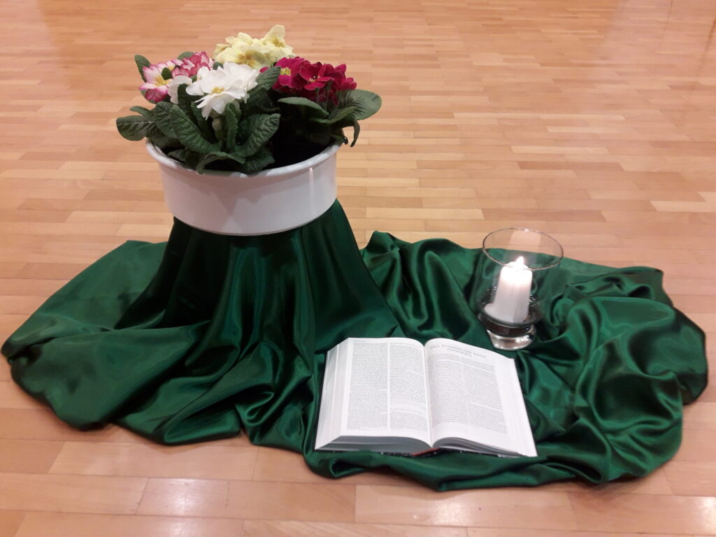 Eine Kerze, aufgeschlagene Bibel und Blumentopf stehen auf einem grünen Samttuch