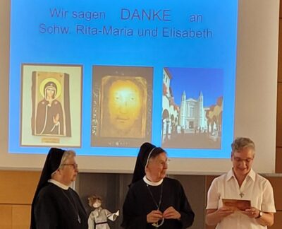 Drei Schwestern sitzen bei der Amtsverabschiedung vor einem Projektor mit Danksage