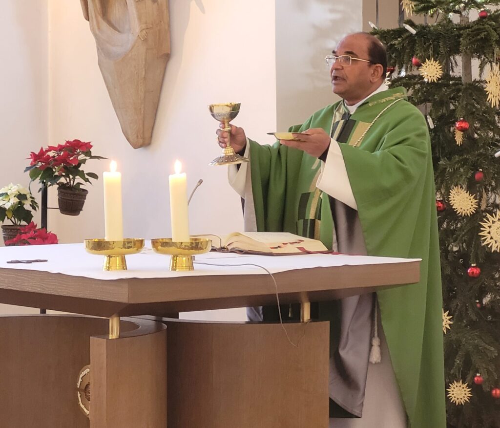 Bischof James steht am Altar und hält den Kelch und die Patene in die Höhe